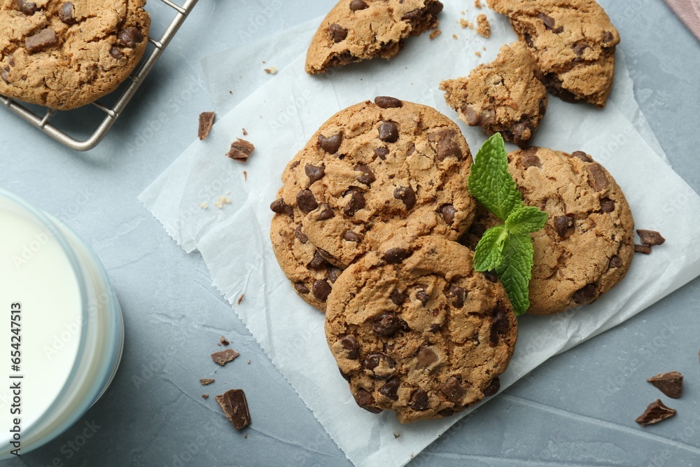 Fototapeta premium Tasty chocolate chip cookies, glass of milk and mint leaves on light grey table, flat lay