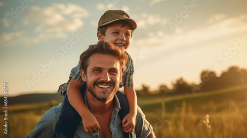 Boy is sitting on man's shoulders. Father with his little son playing on the field