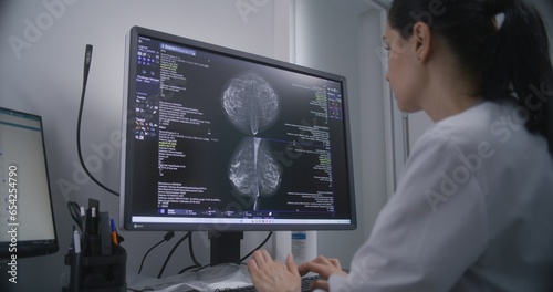 Professional female doctor examines results of mammography screening procedure using computer. Mammogram scans of breast tissues displayed on PC screen. Breast cancer prevention. Hospital or clinic.