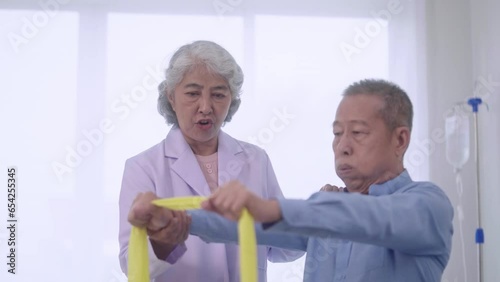 senior Asian women physical therapist caregiver assisting and exercising with mature asian man patient in a physic room with elastic resistance band rehabilitation treatment in a modern hospital. photo