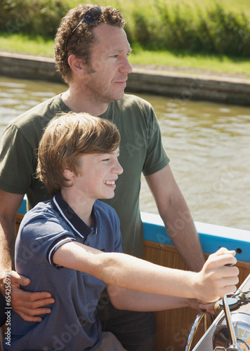 Man and smiling teenaged boy steering a boat
 photo