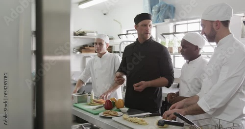 Diverse male chef instructing group of trainee male chefs in kitchen, slow motion