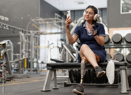 Confident woman with artificial leg sits relax after exercising in fitness gym. Prosthetic limb strengthen physical injury amputee. Asian female with mechanical prosthesis leg workout for wellbeing.