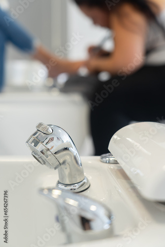 Faucet of a pedicure bathtub seen up close, with a woman doing the pedicure in the background