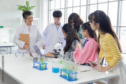 Group of Asian secondary students have fun in science laboratory class with senior 60s teacher wearing lab coat, experience science specialist healthy woman apply job working in modern private school