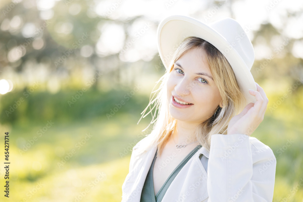 Close up portrait of pretty blond woman in white hat posing in forest. White summer clothes.