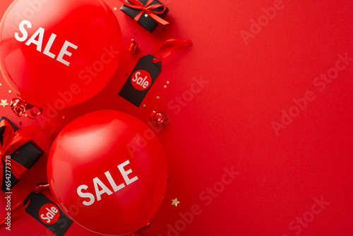 Black Friday kickoff event: Overhead view of black gift boxes, "sale" balloons, price tags, serpentine, and star confetti on a red backdrop, designed for promotional text insertion