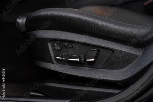Close up of black leather car seat with various buttons for adjusting position. Concept of ergonomic and safety transportation.