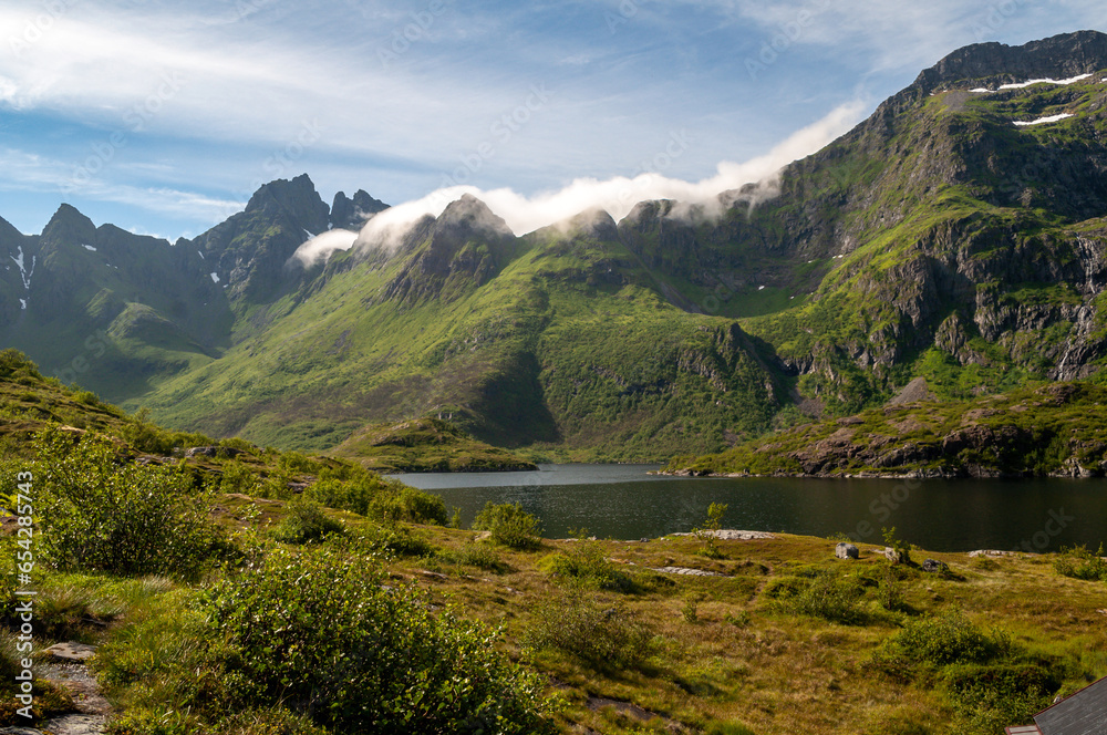 Rocky mountains covered with green grass and a lake in the Lofoten Islands in Norway.