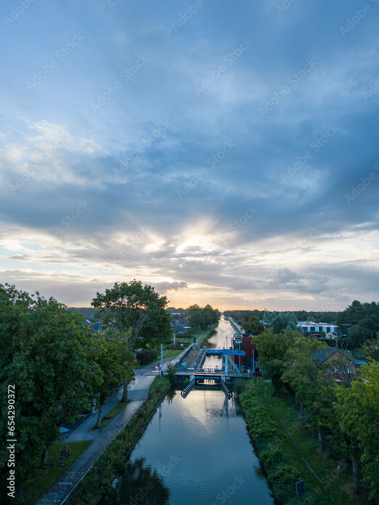 Behold the picturesque town of Rijkevorsel as the sun's first light bathes its historic drawbridge in a warm and enchanting glow. This stunning aerial view captures the timeless beauty of the