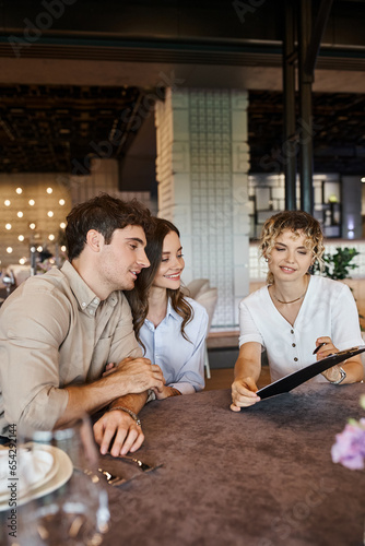 banquet coordinator showing contract to happy couple while sitting at festive table in event hall