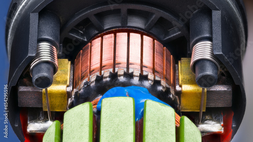 Closeup of electric DC motor rotor with copper winding fixed by blue epoxy in black plastic housing. Commutator with carbon brush contacts pressed by steel cylindric coil springs inside engine detail.