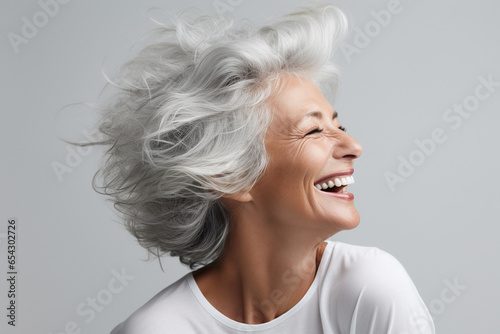 Woman in gray shirt laughs with genuine joy, embodying timeless elegance and happiness. photo