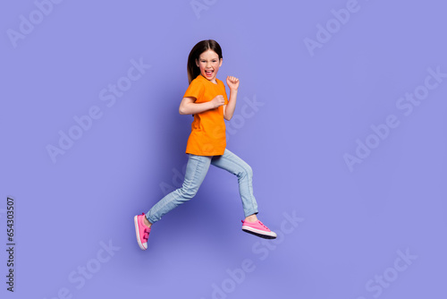 Full length photo of funny positive schoolkid dressed orange t-shirt hurry running to empty space isolated on purple color background