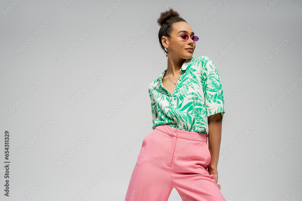 pleased african american woman in pink sunglasses and stylish attire posing on grey backdrop pleased african american woman in pink sunglasses and stylish attire posing on grey backdrop