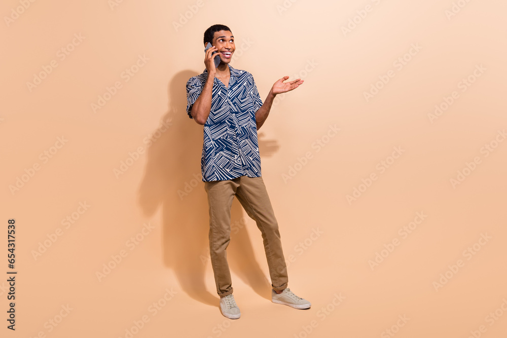 Fototapeta premium Full length photo of excited dreamy man wear print shirt communicating modern gadget empty space isolated beige color background