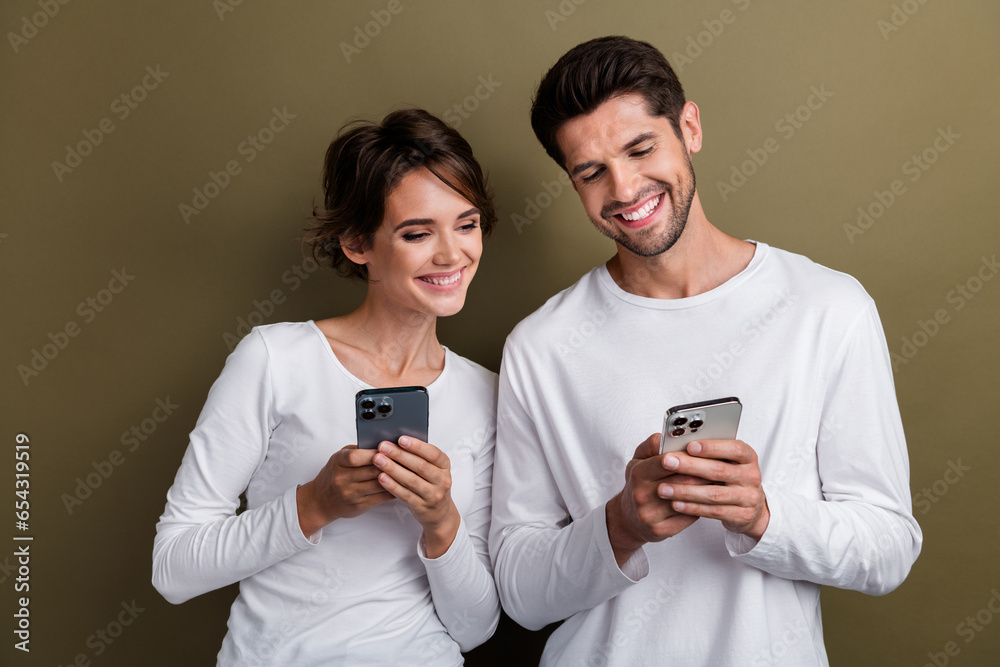 Photo of shiny cheerful married couple wear white shirts online reading messages modern gadgets isolated brown color background Photo of shiny cheerful married couple wear white shirts online reading messages modern gadgets isolated brown color background