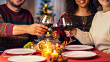 Três pessoas brindando com taças de vinho em uma mesa de jantar luzes de natal no fundo