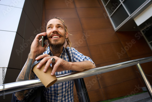 Guy in plaid shirt is onphone outside modern building photo