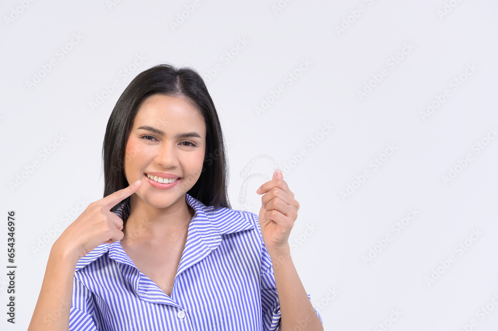 Young smiling woman holding invisalign braces over white background studio, dental healthcare and Orthodontic concept..