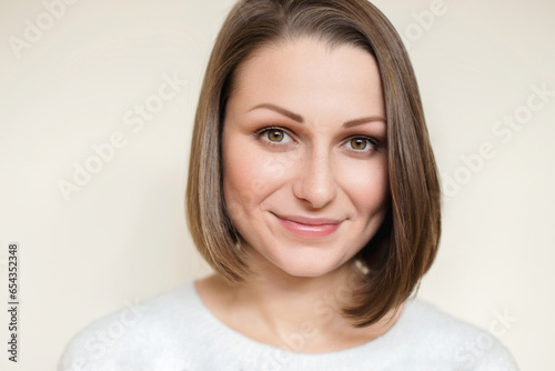 Portrait of a young, beautiful Caucasian woman with a stylish bob haircut, exuding confidence as she smiles at the camera. Clean off-white background.