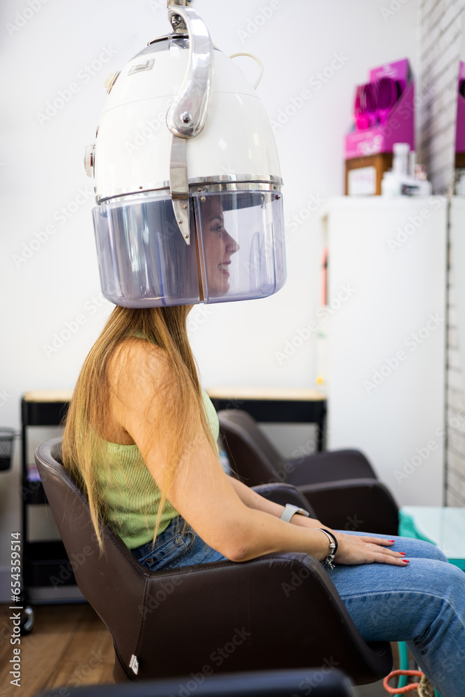 Vertical photo of a pretty woman sitting in a hair salon under a hooded ...