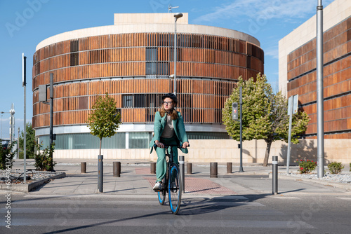 Stylish business woman in green suit and helmet riding her bicycle at the financial district with modern building on the background photo