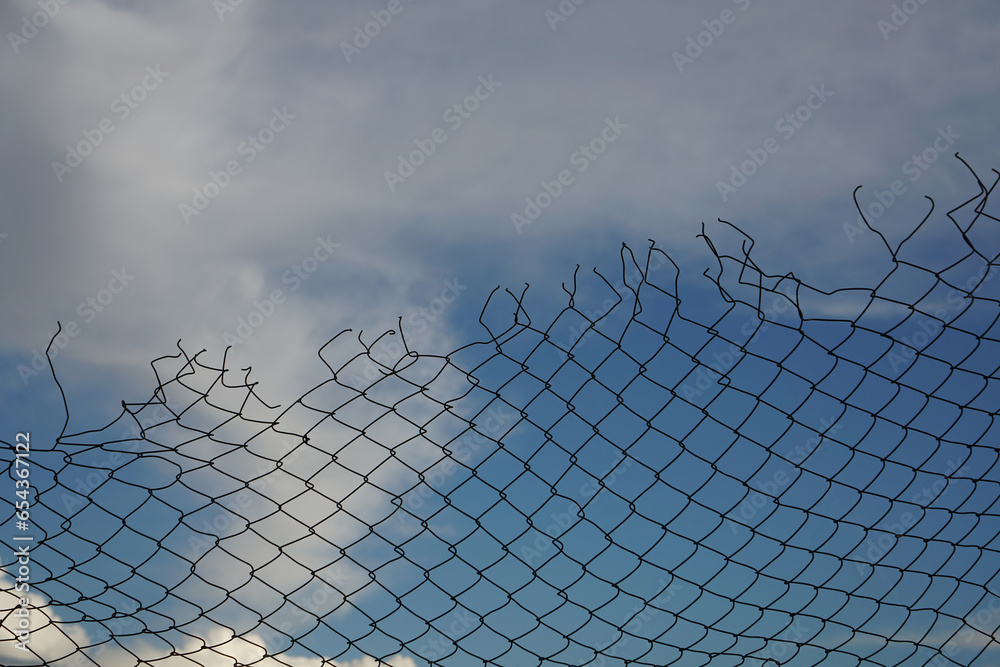 Looking up at a chain link fence with blue sky and clouds. wire fence. Chain link fence see sky. Opening in metallic fence. blue sky. Challenge. breakthrough concept. Chain-link, wire Looking up at a chain link fence with blue sky and clouds. wire fence. Chain link fence see sky. Opening in metallic fence. blue sky. Challenge. breakthrough concept. Chain-link, wire