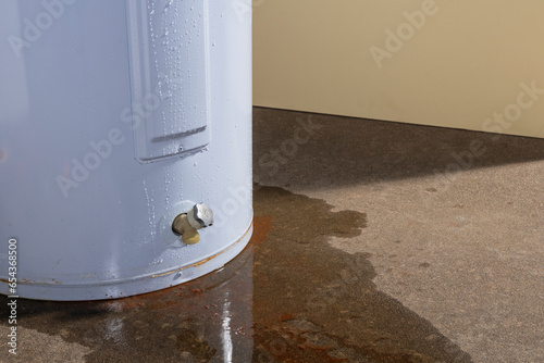 Water leaking from a residential electric water heater sitting on a concrete floor with signs of rust and iron staining the floor. photo