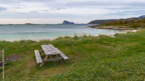 Seating area at Sommarøya beach, BBQ area on the shore of the North Atlantic, in Troms, Norway. wooden park bench with table, Dining table with attached seats on meadow, outdoor area on the seashore