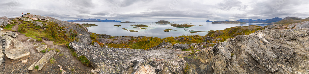 Blick über die Inseln von Sommarøy und Hillesøy mit Häuser, Brücke, Felsen, Wiesen und Strand, Ufer und Berg, Frau auf dem Berg in Norwegen. Panorama am sonnigen Herbsttag