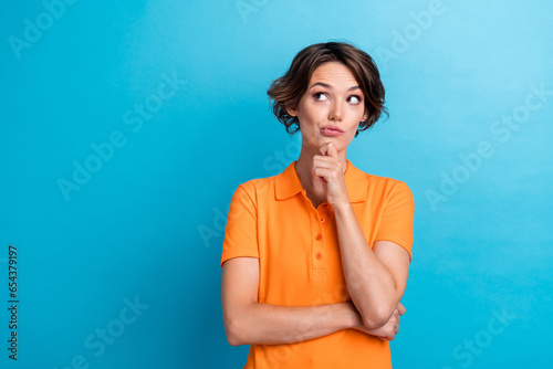 Photo of doubtful unsure lady wear orange t-shirt arm chin looking empty space isolated blue color background