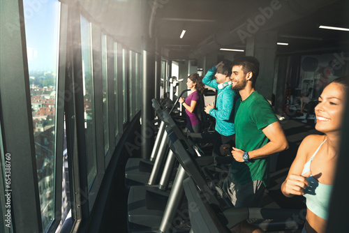 Side view of athletic people running on treadmills in a gym. Group of young athletes practicing cardio in modern indoor space with a view.