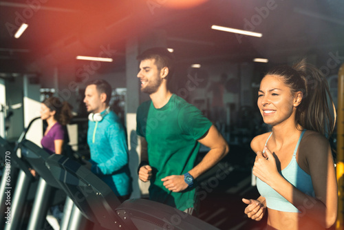 Side view of athletic people running on treadmills in a gym. Group of exhausted young friends doing cardio exercises in the morning.