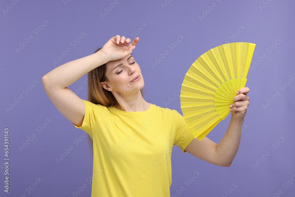 Beautiful woman waving yellow hand fan to cool herself on violet background Beautiful woman waving yellow hand fan to cool herself on violet background