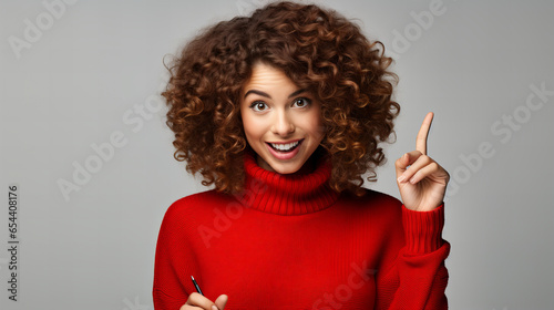 Young woman with curly hair and in red sweater smiling and showing with her hand finger on the top, advertisement concept,  copy space isolated white background  © Viktorikus
