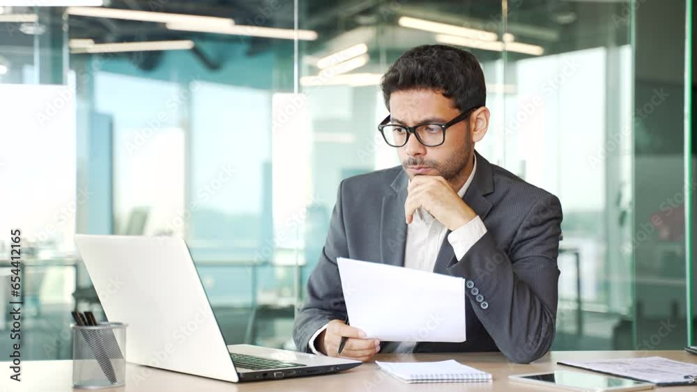 Young thoughtful financier in a formal suit busy with paper work while sitting at workplace. Serious accountant making financial calculations, preparing accounts, typing on laptop in business office Young thoughtful financier in a formal suit busy with paper work while sitting at workplace. Serious accountant making financial calculations, preparing accounts, typing on laptop in business office