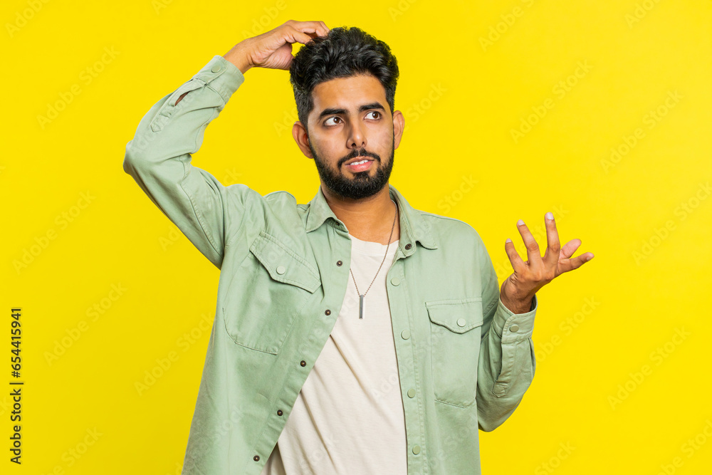 I don't know what to say. Confused Indian young man feeling embarrassed about ambiguous question, having doubts, no answer, idea, being clueless, uncertain. Guy isolated on yellow studio background - obrazy, fototapety, plakaty 