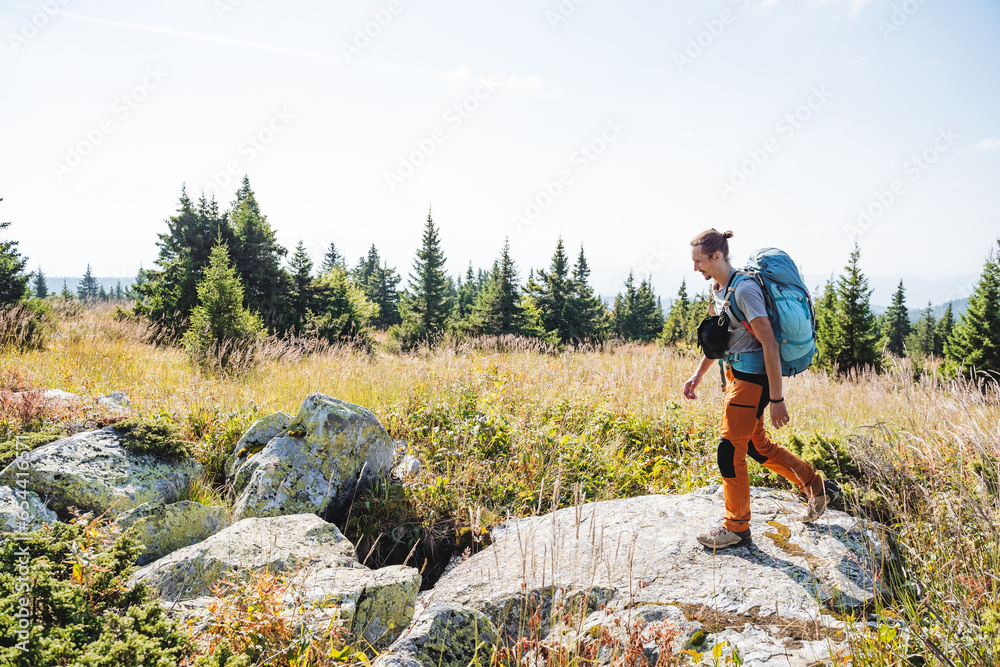 A hiker with a backpack walks on a large stone, trekking alone, camping equipment for a long trip, a heavy backpack.