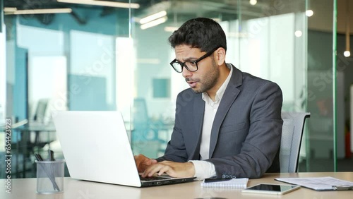 Wallpaper Mural Happy young businessman in a formal suit received great news on laptop computer while sitting at workplace at desk in business office. Smiling entrepreneur reads a pleasant message, celebrates success Torontodigital.ca