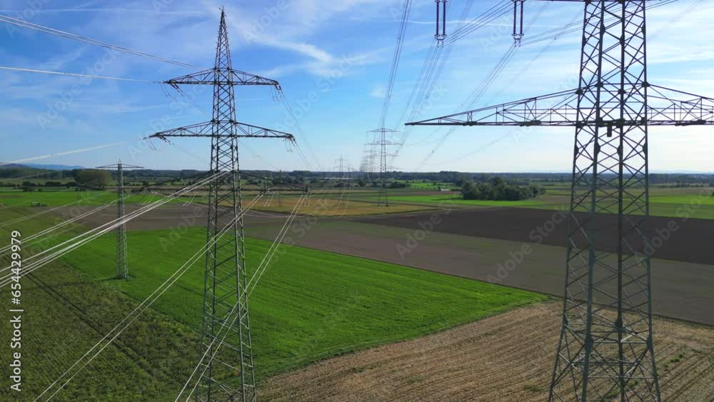 Flug mit einer Drohne durch zwei Hochspannungsmasten mit Stromleitungen über landwirtschaftlichen Feldern