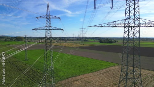 Flug mit einer Drohne durch zwei Hochspannungsmasten mit Stromleitungen über landwirtschaftlichen Feldern