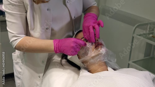Cosmetologist applying cream with anesthesia on patient's face, portrait closeup view. Preparing skin for biorevitalization or thread lifting procedure. Woman in beauty clinic with doctor beautician.