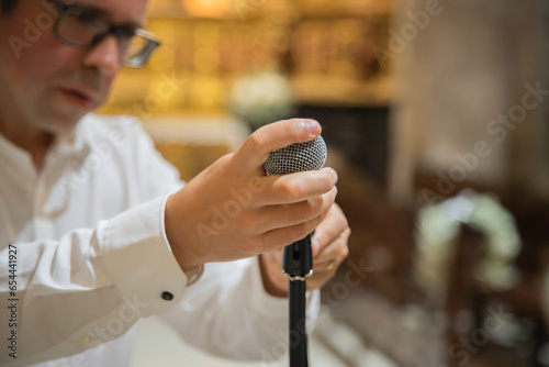 Man holding and preparing microphone to use in musical performance. Rustic interior environment, example temple or church. Close up