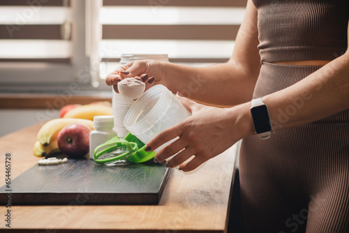 Obraz na płótnie Athletic woman in sportswear with measuring spoon in her hand puts portion of wh