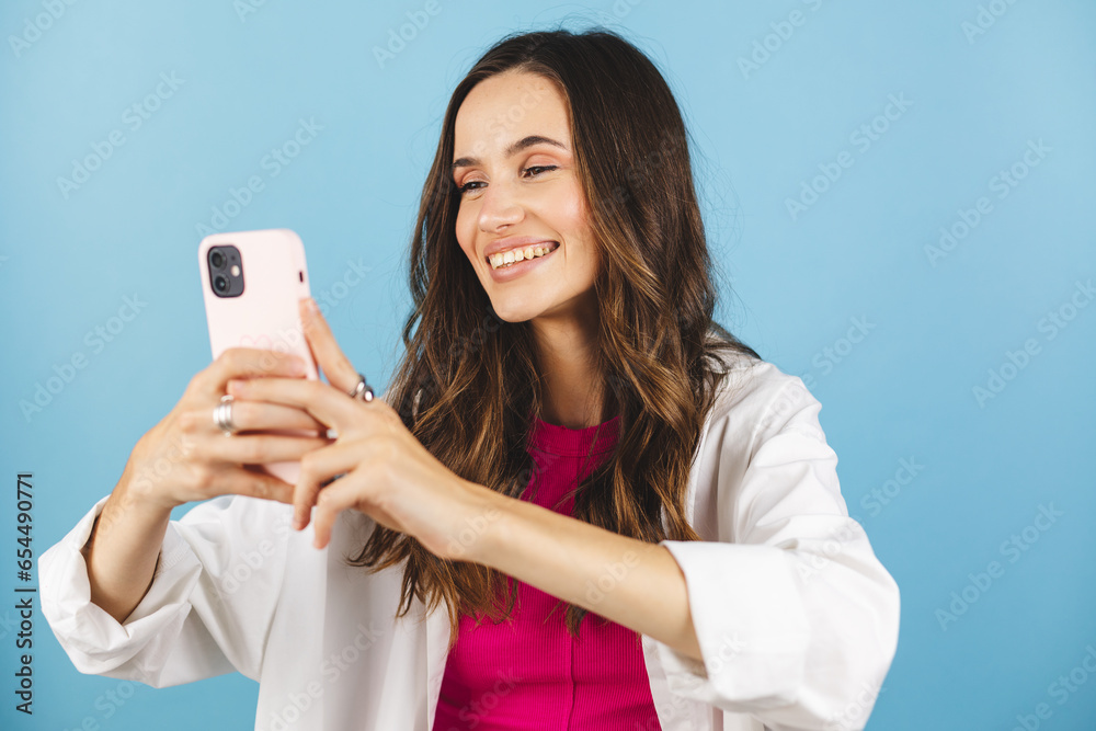 Happy carefree woman messaging. Smiling woman holding mobile phone device, doing commerce online shopping on cell, using apps on cellphone standing isolated on blue background, scrolling and typing. Happy carefree woman messaging. Smiling woman holding mobile phone device, doing commerce online shopping on cell, using apps on cellphone standing isolated on blue background, scrolling and typing.