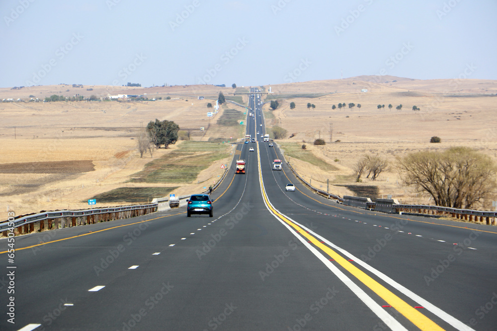 Naklejka premium The N3 freeway from Johannesburg to Durban in South Africa, straight road to the horizon over dry landscape with cars and trucks from drivers point of view