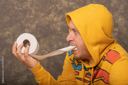 Greedy guy eats toilet paper. A man in a yellow sweater stuffed toilet paper into his mouth.