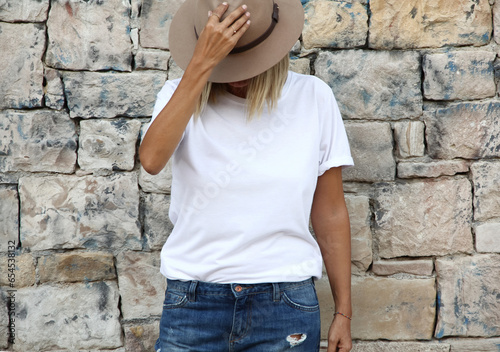 Girl wearing blank white tshirt with copy space for your text or design. White t-shirt mock up with hat on natural stone wall background