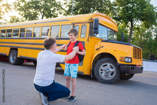 dad accompanies the child to the school bus. father communicates with son schoolboy in front of yellow bus